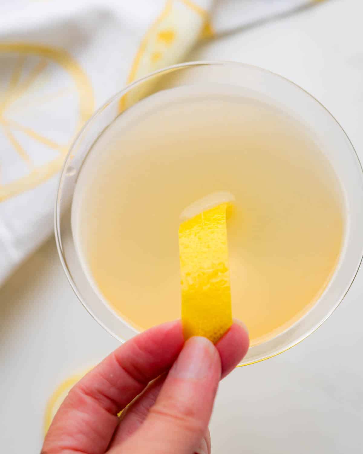 Adding a lemon peel to garnish the gin cocktail.