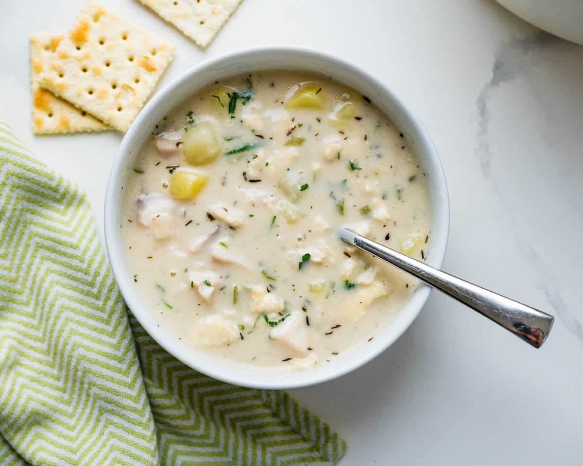 A bowl of fish chowder with saltines on the side.