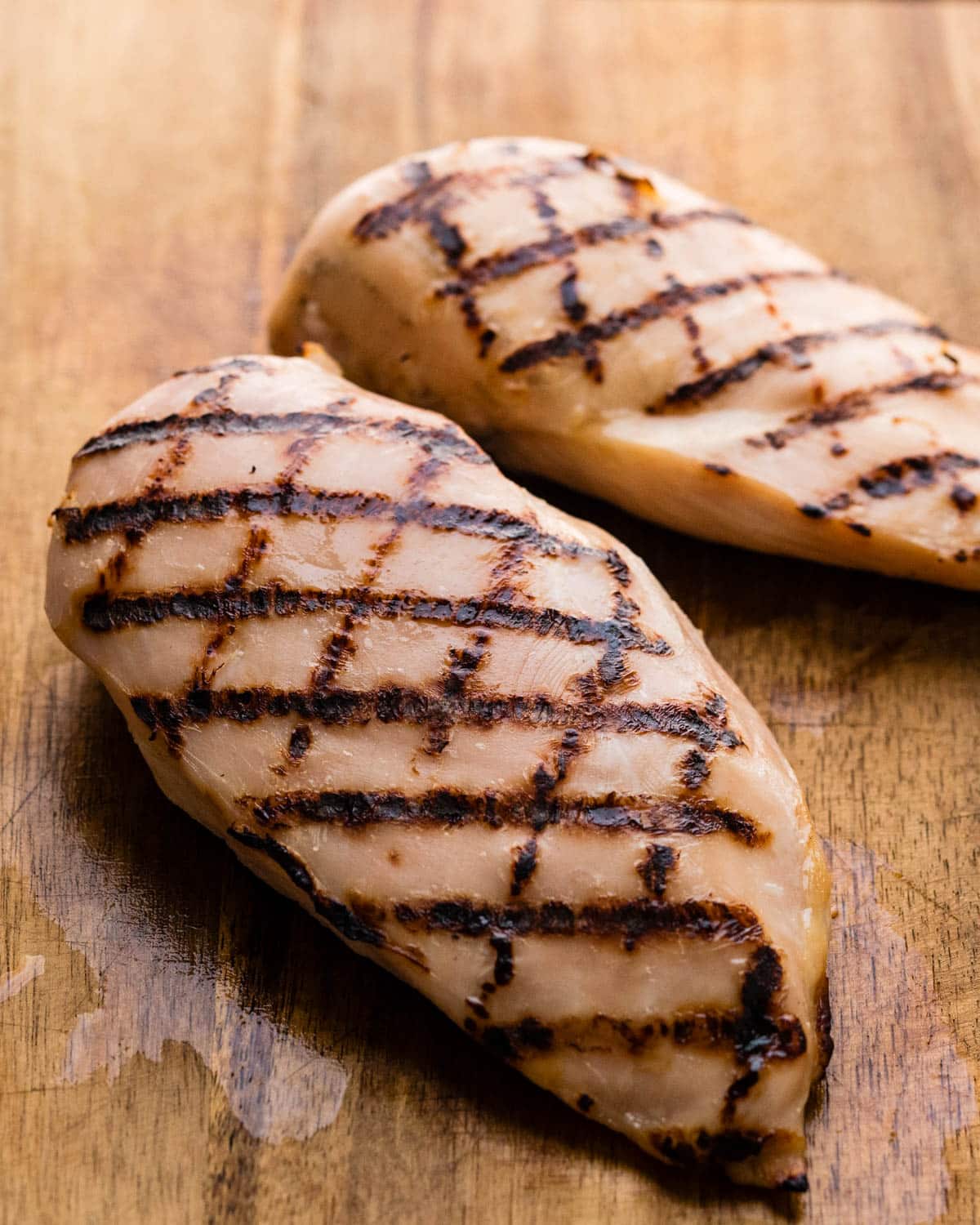 Two brined grilled chicken breasts resting on a cutting board.